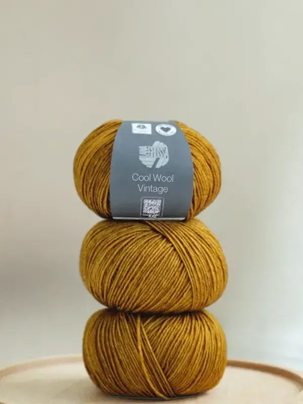 A stack of three golden-mustard Lana Grossa Cool wool vintage skeins with a product label on the top one.