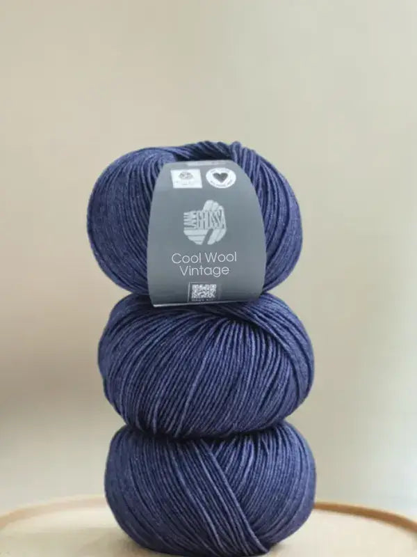 Three stacked balls of dark blue Lana Grossa Cool wool vintage merino wool yarn with a product label on the top ball.