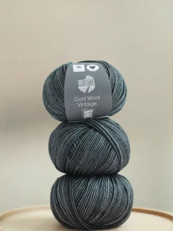 Three balls of Lana Grossa Cool wool vintage dark grey yarn stacked vertically.