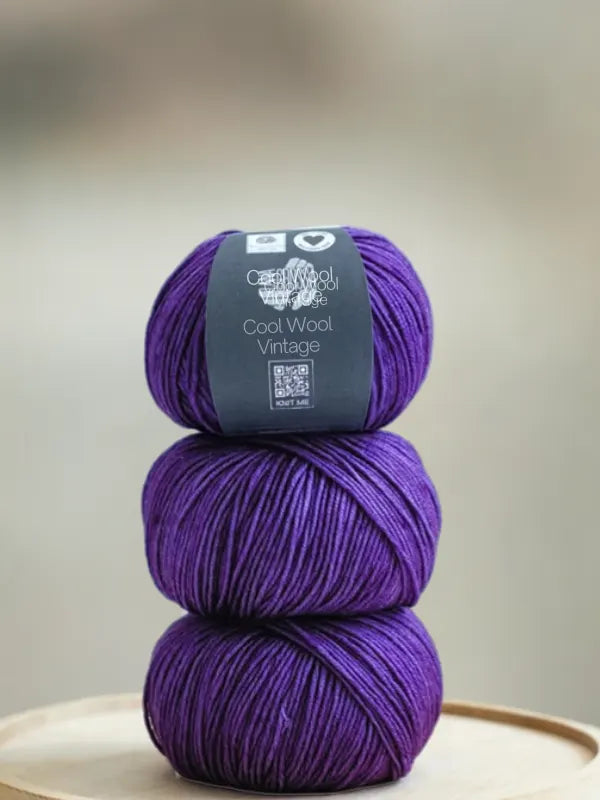 Three stacked balls of vibrant purple Lana Grossa Cool wool vintage yarn, with a label around the top ball.