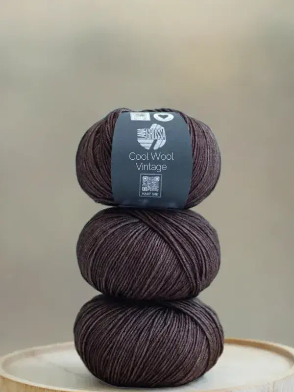 Three balls of Lana Grossa Cool wool vintage yarn in dark brown stacked vertically.