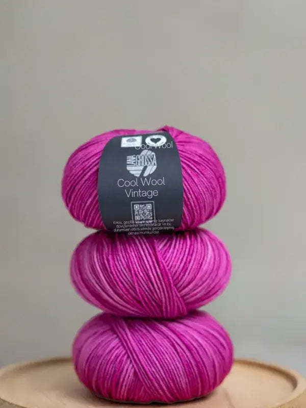 Three stacked balls of fuchsia and white Lana Grossa Cool wool vintage merino yarn, with a paper label on the top ball.