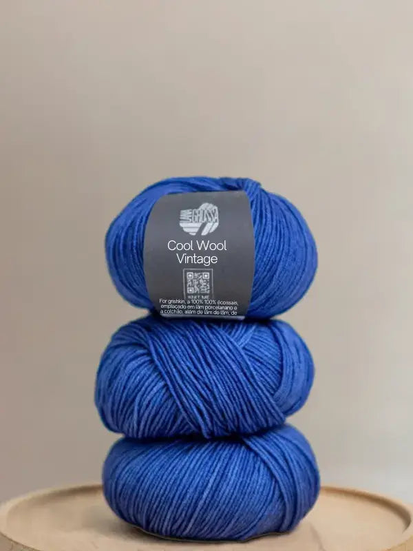 Three stacked balls of vibrant blue Lana Grossa Cool wool vintage yarn with a paper label wrapped around the top ball.