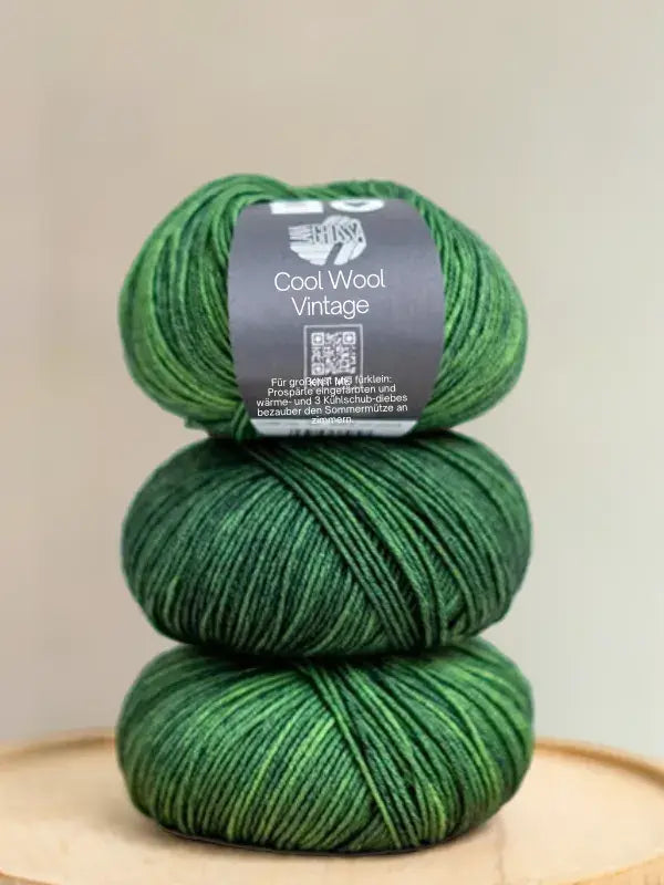 Three skeins of variegated green Lana Grossa Cool wool vintage yarn stacked vertically, with a label on the top skein.