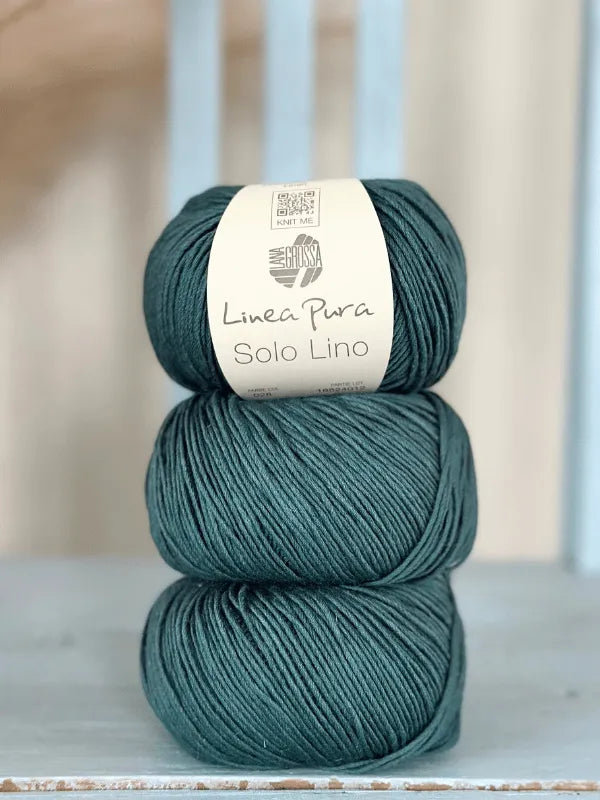 Three teal balls of Lana Grossa Solo Lino, a vegan yarn, are neatly stacked on a light blue surface with a softly blurred background.