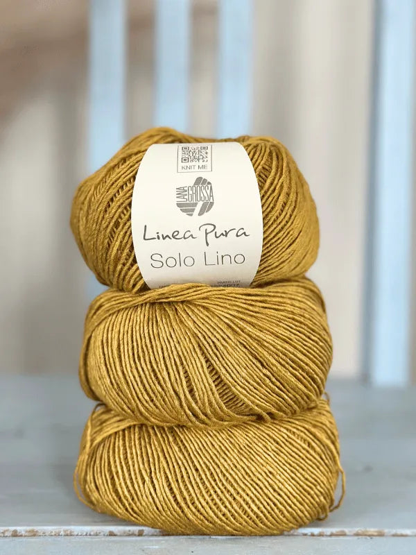 Three balls of mustard yellow Lana Grossa Solo Lino, a soft and smooth vegan linen yarn, are stacked vertically on a light blue wooden surface. The top ball has its label visible.