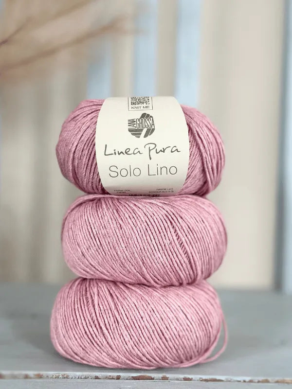 Three skeins of pink Lana Grossa Solo Lino, a vegan yarn, are stacked with a white label on the top skein, set against a soft neutral background.