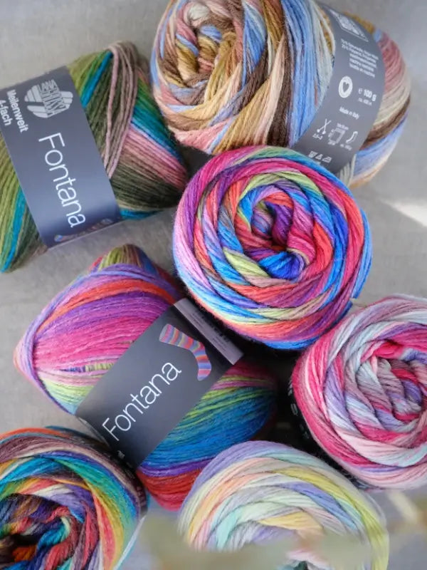 Six skeins of Lana Grossa Meilenweit 100 Fontana yarn in a mix of vibrant shades—pink, blue, green, and yellow—are neatly grouped together. Each label features a sock illustration, making them ideal for your next sukkalanka project.