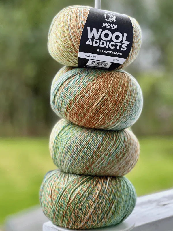Four balls of Lang Yarns Wool Addicts Move 4 yarn in green, tan, and white are stacked vertically outdoors. The top ball’s label is visible, with blurred greenery in the background. These feature merinovilla and sukkalanka blends.