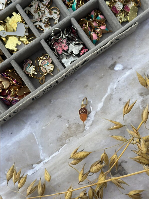 A tray of colorful KNITS by cindy ekman silmukkamerkit sits on marble. A potion bottle-shaped, gold-accented marker rests beside dried wheat-like stems, set apart from the others.