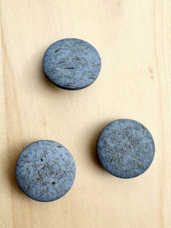 Three round, dark gray Kierrätysnappi kookos 20mm (0454241) buttons with textured surfaces are arranged in a triangular pattern on a light wooden surface.