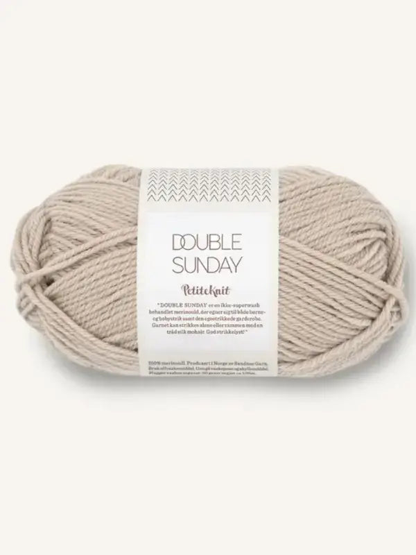 A skein of light beige Sandnes Garn Double Sunday merino wool yarn wrapped in a paper label featuring a chevron pattern and product information.