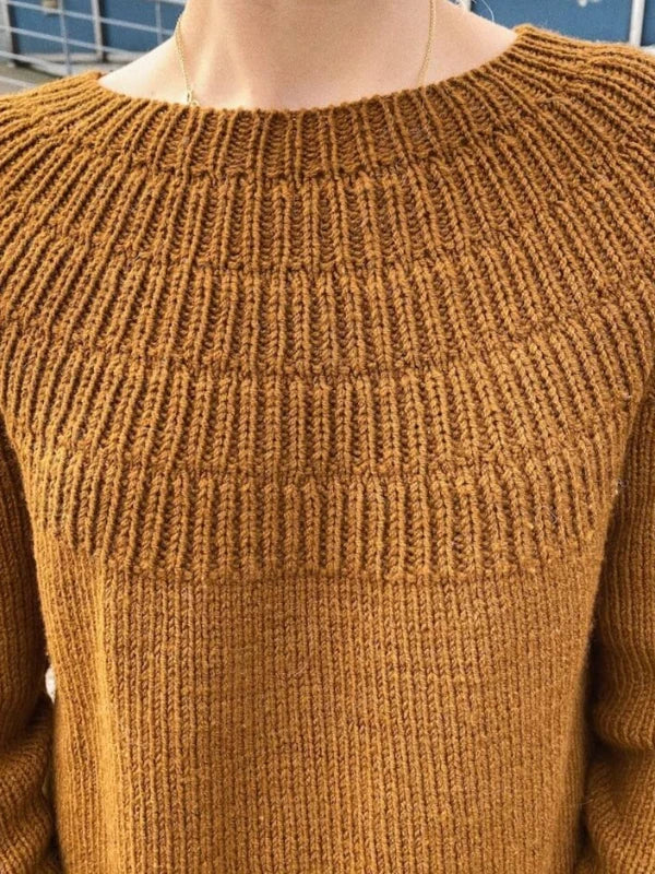 A close-up of a person wearing a mustard yellow knitted sweater with a textured yoke pattern and round neckline, crafted using the PetieKnit Anker’s Sweater - My Size neuleohje - Suomi, ideal for those looking for a suomenkielinen printti.