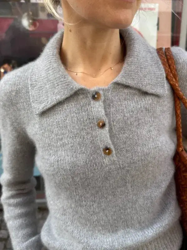 Wearing the PetiteKnit Petra Polo Neuleohje— a soft, light gray, long-sleeve knit sweater with a wide collar and three brown buttons — this person carries a brown textured bag over their shoulder.