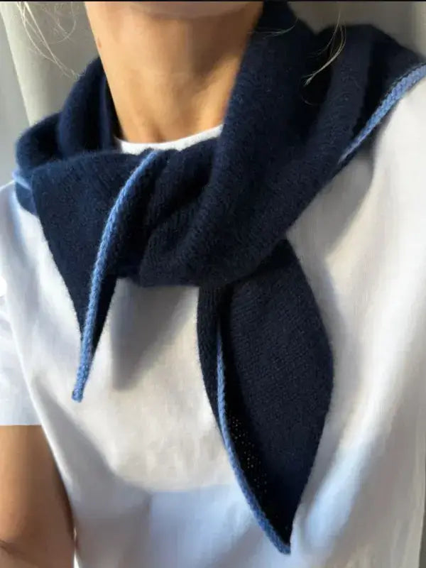 A person wearing a white shirt has a navy blue PetiteKnit Uma Scarf neuleohje with light blue edges tied loosely around their neck.