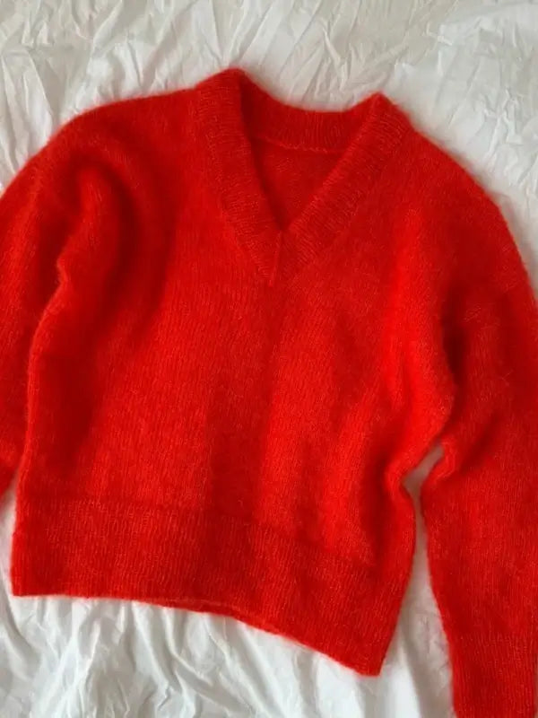 A vibrant red, fuzzy V-neck sweater—expertly knit in the Petiteknit Stockholm Sweater V-neck neuleohje, Suomi style using soft silkkimohair yarn—is laid flat on a slightly wrinkled white fabric background, evoking the inspiration of a Scandinavian knitting guide.