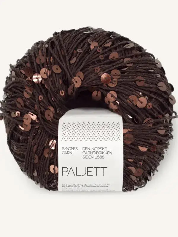 A round skein of dark brown Sandnes Garn Paljett yarn covered in metallic copper sequins, with a white paper label showing brand information and text.