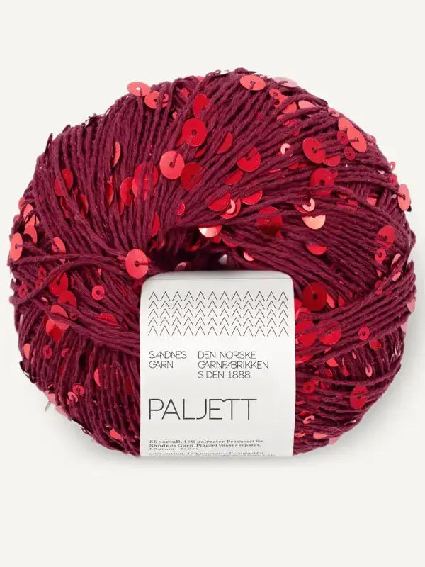 A ball of deep red Sandnes Garn Paljett yarn embellished with matching sequins, featuring a product label with brand information and the text PALJETT.