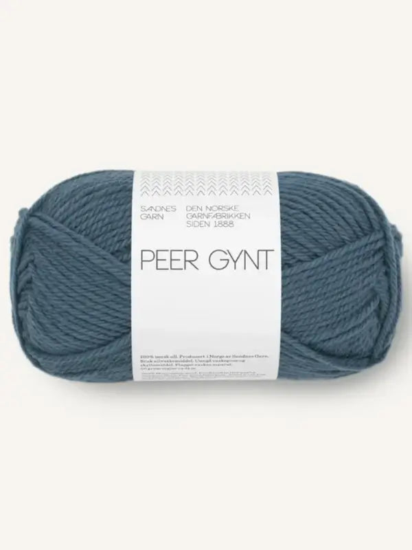 A skein of Sandnes Garn Peer Gynt, in a blue shade, rests on a white background. The label, adorned with Norwegian text and decorative accents at the top, emphasizes the quality of this Norjalainen villa lanka (Norwegian wool yarn).