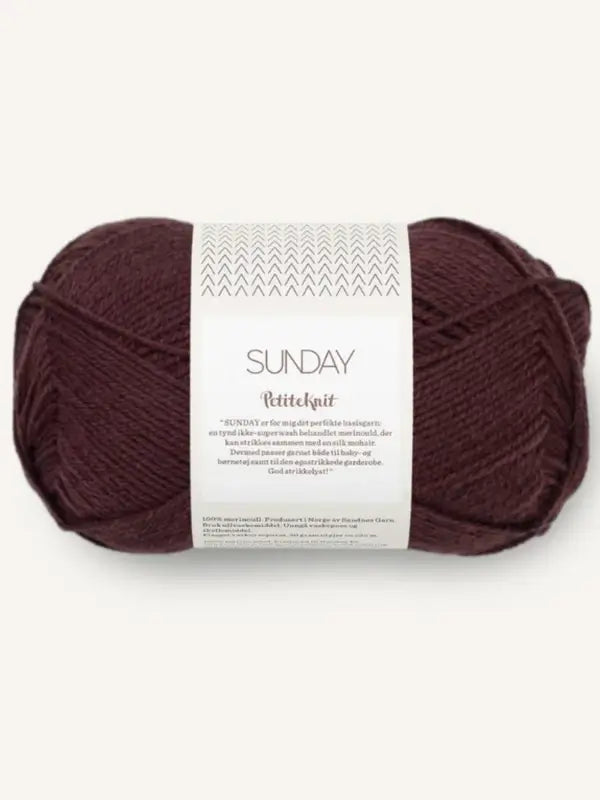 A skein of deep burgundy merinovillalanka yarn labeled Sandnes Garn Sunday from PetiteKnit, featuring a white band with text and small decorative patterns, is set against a plain light background. This fingering-vahvuinen yarn is mulesing-vapaa, ensuring both quality and ethical sourcing.