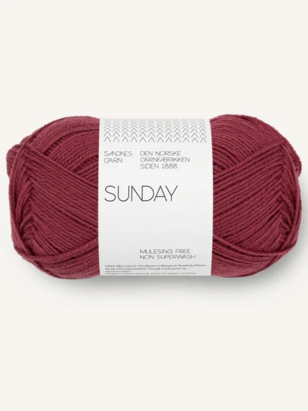 A skein of Sandnes Garn Sunday yarn in deep red, labeled in Norwegian, made from mulesing-vapaa merinovilla and non superwash. This fingering-weight yarn is neatly wound and set against a neutral background.