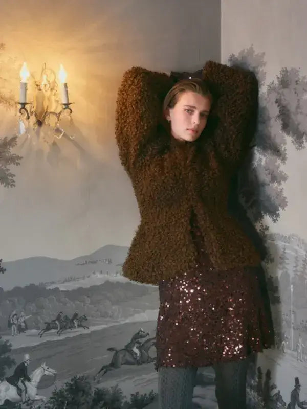 A woman wears a brown fuzzy textured jacket over a dark Sandnes Garn Vea Skirt – neulesetti Paljett.