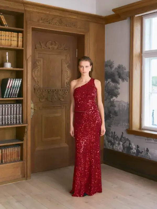 A person wearing a floor-length, one-shoulder red sequin gown inspired by the Sandnes Garn Vale Top – neulesetti Paljett aesthetic.