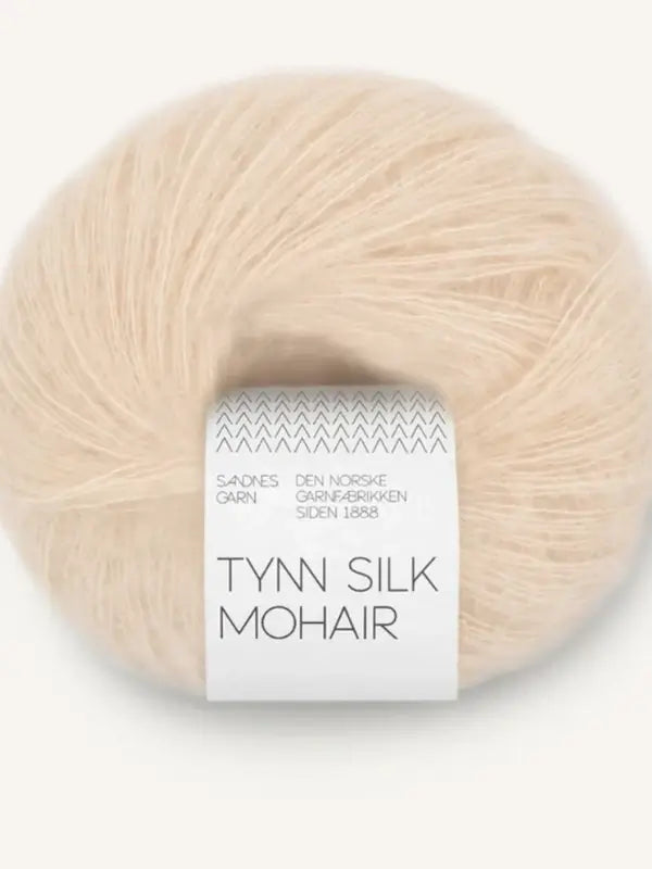 A ball of light beige Sandnes Garn Tynn Silk Mohair yarn, with a white band featuring Norwegian text, is luxurious and ideal for delicate, elegant knitting projects.