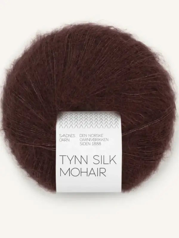 A ball of Sandnes Garn Tynn Silk Mohair yarn in dark brown, wrapped in a white paper band adorned with text and patterns, highlights the luxurious texture of this silk-mohair blend.