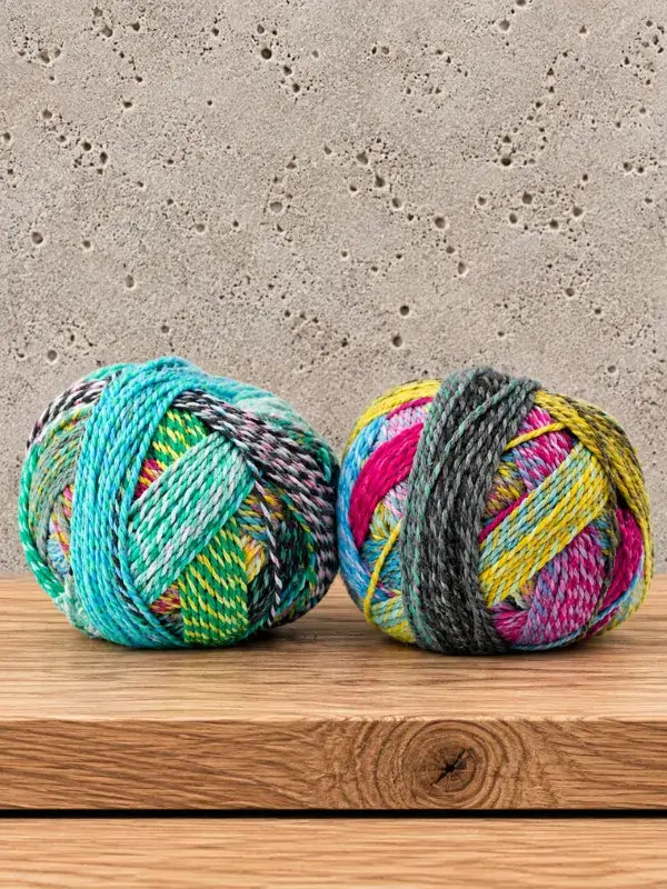 Two balls of Schoppel-Wolle Edition 3, a variegated yarn, sitting on a wooden surface.