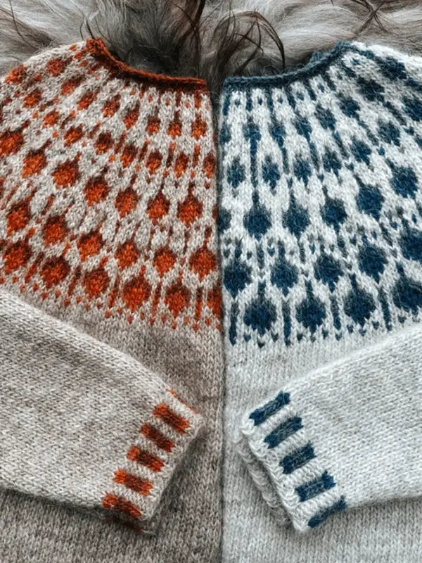 Two Sisu Knitwear Mustikkaneule sweaters lie side by side: one in beige with orange accents, the other white with dark blue. Both have matching Nordic geometric designs near the collars and cuffs. PDF knitting instructions available in Finnish.