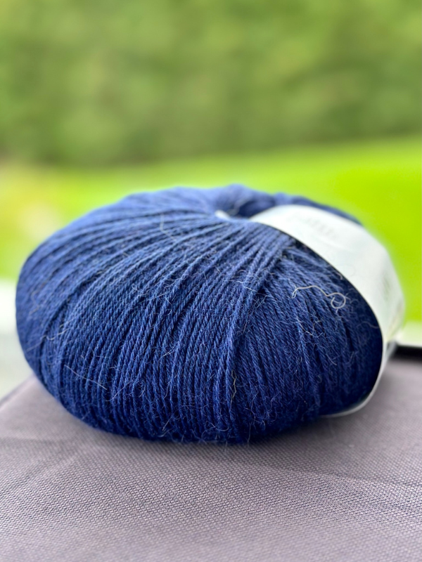 A close-up of Lang Alpaca Soxx 4ply yarn from the Mittums lapasten ohje (PDF) set resting on a surface, with a blurred green outdoor background.