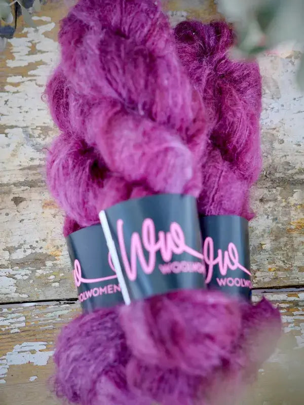 Two hanks of bright magenta WoolWomen Fluff Mohair yarn bound by a black paper label.