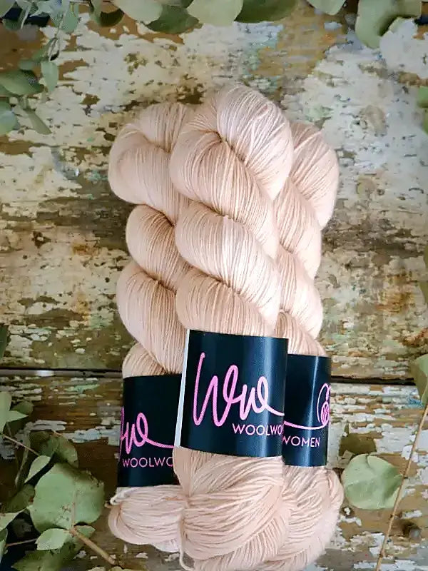 Two skeins of light peach-colored WoolWomen Merino Sock yarn wrapped with branded black labels.