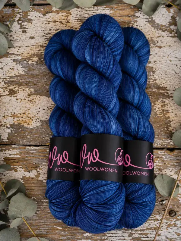 Three skeins of WoolWomen Merino Sock yarn in deep blue, wrapped in paper bands.