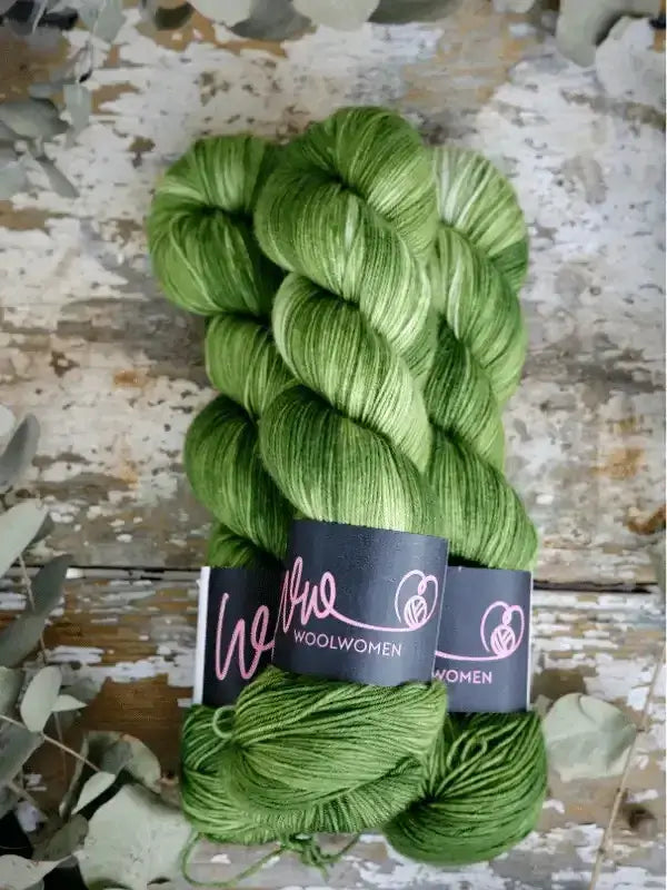 Two skeins of WoolWomen Merino Sock yarn in variegated green hand-dyed superwash merino wool with black paper labels.
