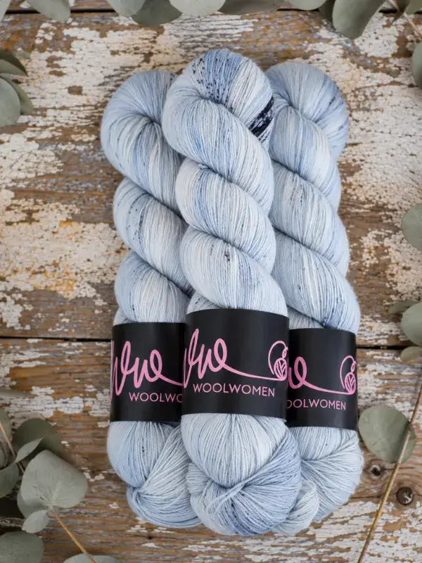 Three skeins of WoolWomen Merino Sock in light blue speckled superwash merino wool with black paper labels.