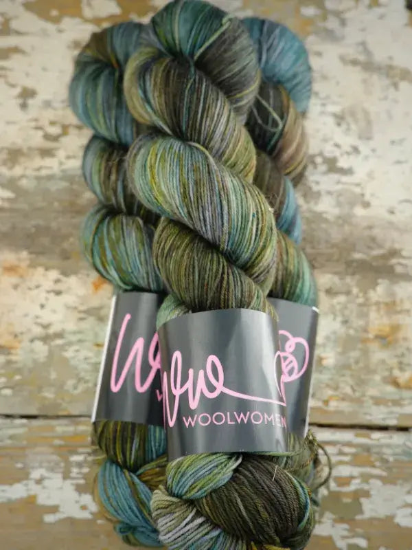 Two twisted hanks of WoolWomen Merino Sock in shades of green, blue, and brown, held together by a black paper label.