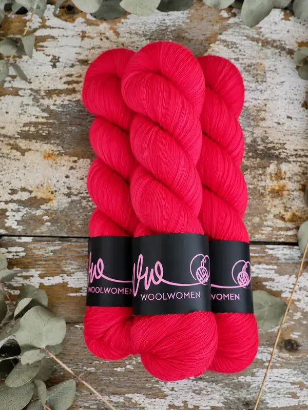 Three skeins of bright pink WoolWomen Merino Sock yarn secured with branded paper bands.