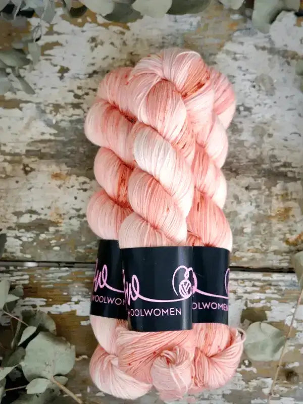 Two skeins of WoolWomen Merino Sock yarn in variegated light peach with a dark band around the center.