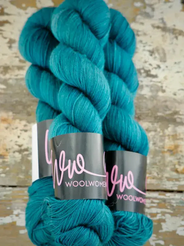 Two skeins of deep teal WoolWomen Merino Sock hand-dyed yarn with black paper labels.