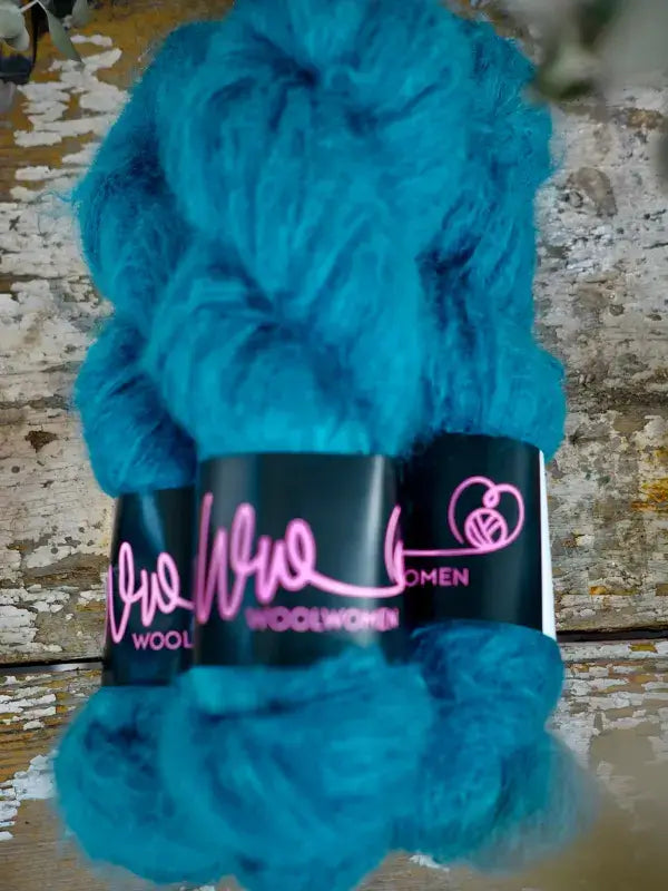 A skein of WoolWomen Fluff Mohair in fluffy, bright turquoise, secured with a black paper label.