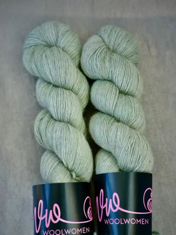 Two skeins of pale green baby alpakka yarn with WoolWomen AlpaLux labels rest side by side on a gray surface, offering a ylellinen lanka perfect for your next luxurious project.