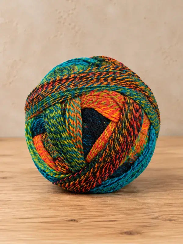 A ball of Schoppel wolle Zauberball crazy yarn featuring variegated shades of blue, orange, green, and black.