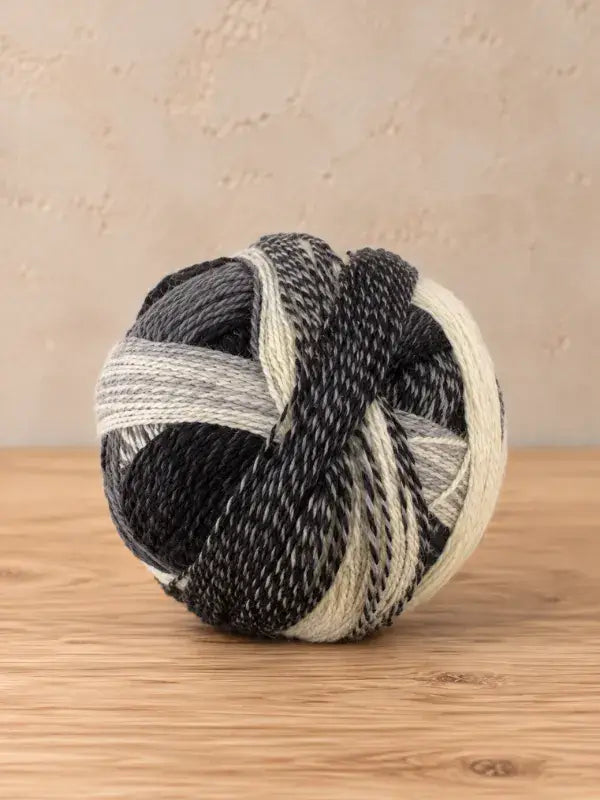 A round ball of Schoppel wolle Zauberball crazy variegated yarn featuring a mix of black, grey, and cream colors.