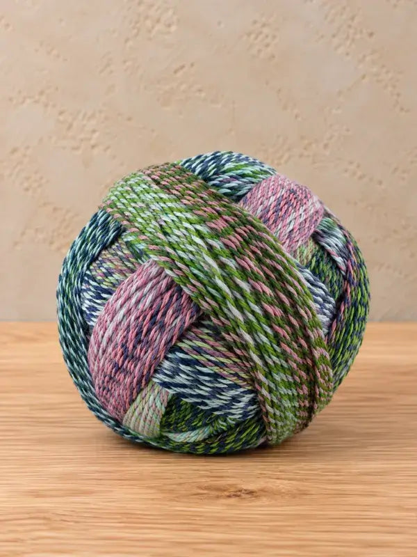 A round ball of Schoppel wolle Zauberball crazy yarn in shades of green, blue, and pink.