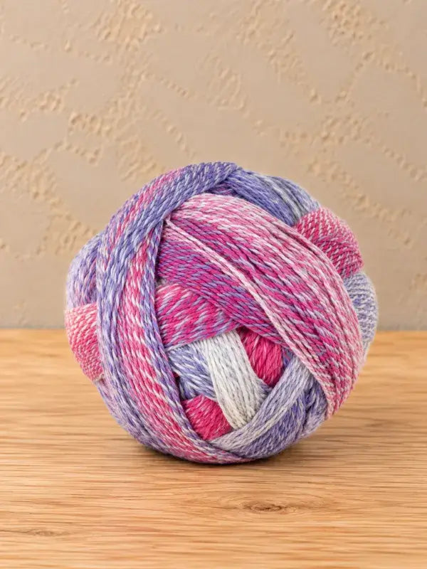 A round ball of Schoppel wolle Zauberball crazy variegated yarn in shades of pink, purple, and white.
