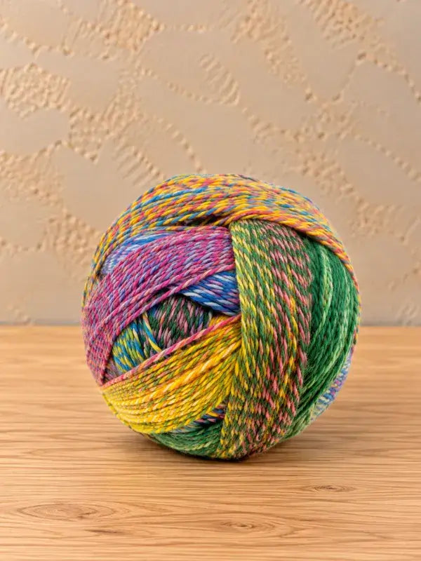 A ball of multicolored Schoppel wolle Zauberball crazy yarn with variegated sections of green, yellow, pink, and blue.
