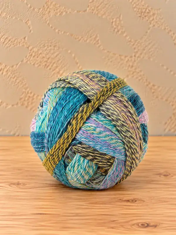 A Schoppel wolle Zauberball crazy ball of variegated yarn featuring shades of blue, green, yellow, and pink, wound with multiple strands.