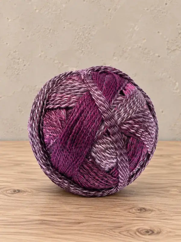 A ball of Schoppel wolle Zauberball crazy yarn in shades of purple, magenta, and white.